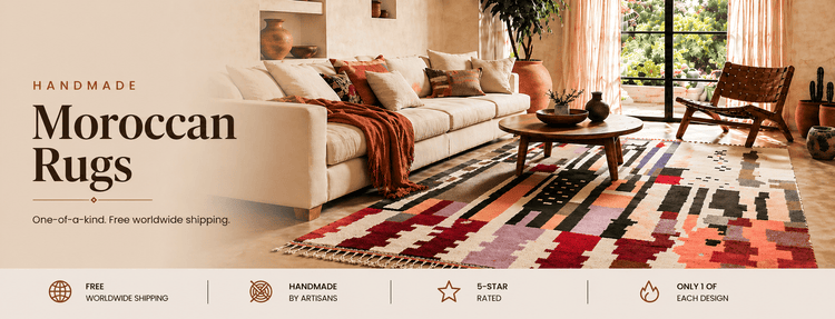 A beautifully styled living room featuring a large, colorful handmade Moroccan rug with geometric patterns, a beige sofa, and wooden coffee table. Text overlay: "Handmade Moroccan Rugs - One-of-a-kind. Free worldwide shipping."