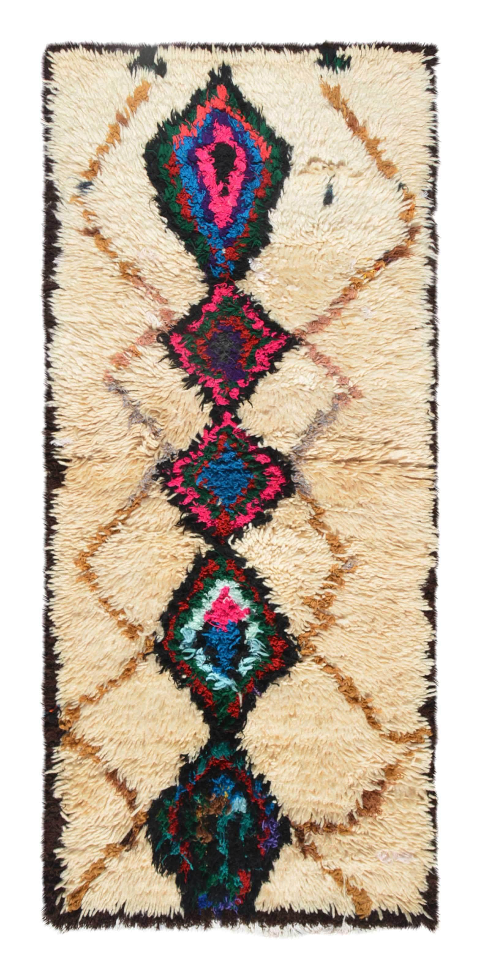 Overhead view of a deeply plush, vibrant handmade 1960s vintage Azilal Moroccan wool and cotton accent rug named In The Crowd (2'4" x 5'4") featuring a cream base with a faint tan lattice background, dominated by a central column of massive black diamond medallions filled with bright pink, blue, green, and red yarn, with a 3/4-inch pile.