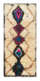 Overhead view of a deeply plush, vibrant handmade 1960s vintage Azilal Moroccan wool and cotton accent rug named In The Crowd (2'4" x 5'4") featuring a cream base with a faint tan lattice background, dominated by a central column of massive black diamond medallions filled with bright pink, blue, green, and red yarn, with a 3/4-inch pile.