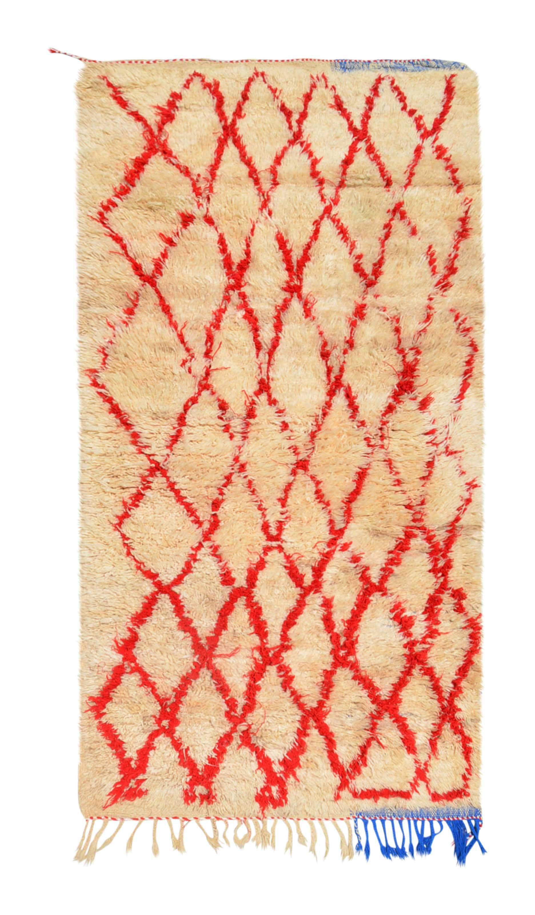Overhead view of a deeply plush, cozy handmade 1970s vintage Beni Ourain Moroccan wool and cotton accent rug named Feel Home (3'2" x 6') featuring a thick cream base covered in a wandering geometric diamond lattice woven in bright cherry red yarn, with a quirky pop of blue fringe at the bottom right corner, and a 1-inch pile.