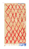 Overhead view of a deeply plush, cozy handmade 1970s vintage Beni Ourain Moroccan wool and cotton accent rug named Feel Home (3'2" x 6') featuring a thick cream base covered in a wandering geometric diamond lattice woven in bright cherry red yarn, with a quirky pop of blue fringe at the bottom right corner, and a 1-inch pile.